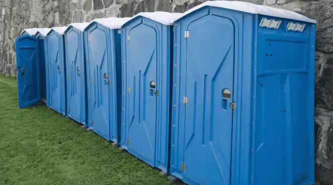 Row of blue portable toilets lined up on grass against a stone wall for event sanitation in Phoenix, AZ